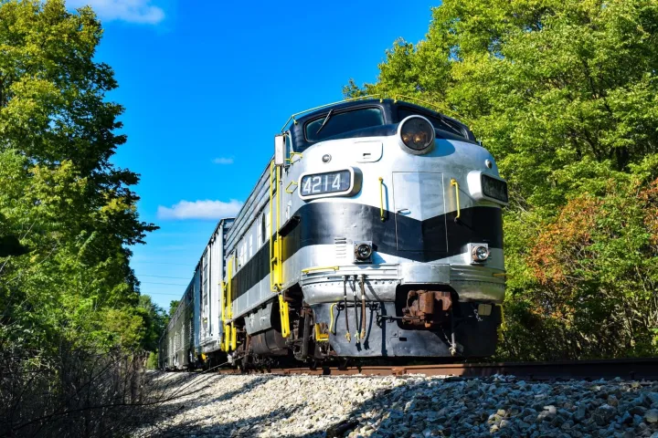 a train traveling down train tracks near a forest with Mission Point Light in the background
