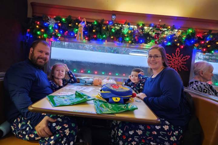 Family in matching pajamas at a decorated table with holiday lights.