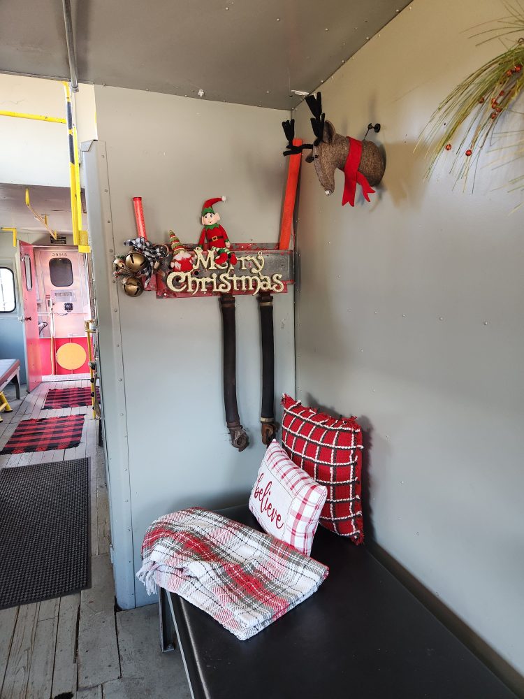 Festive decor with a 'Merry Christmas' sign, reindeer, and plaid pillows in a hallway.