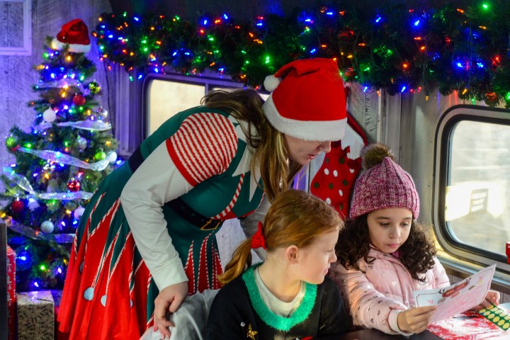 Children reading with a woman in a Santa hat on a decorated train.