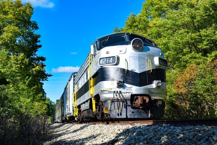 a train traveling down train tracks near a forest with Mission Point Light in the background
