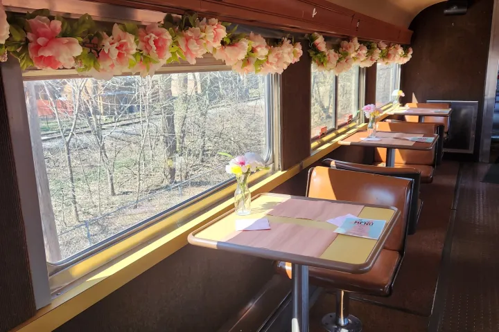 Train dining car with floral decorations, tables, leather seats, and outside view.