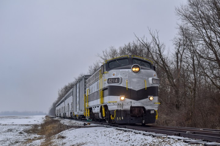 Vintage train on snowy tracks with bare trees in winter landscape.