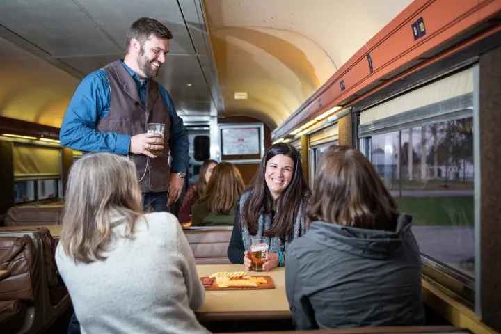 Four people enjoy drinks and snacks at a table inside a train car.
