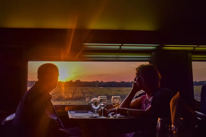 Silhouetted couple dining on train with sunset view through window.