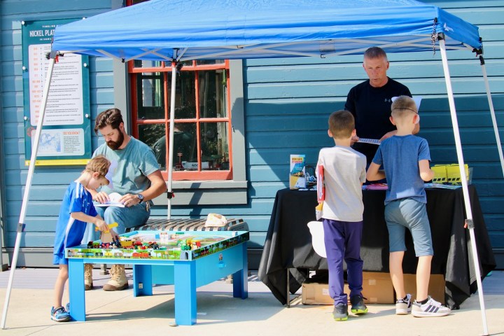 Children play with a model train set under a blue canopy tent.