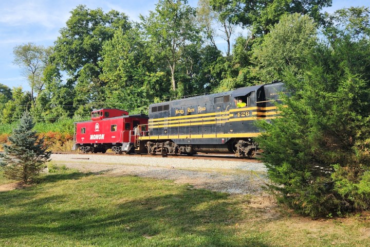 Red and black vintage train on tracks with trees in the background.