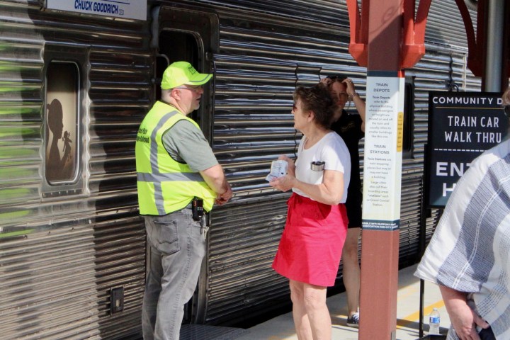 People stand near a train at Hobbs station, one in a hi-vis vest.