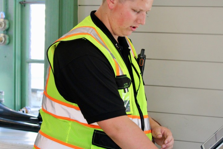 Man in safety vest at counter with computer and stuffed toy.