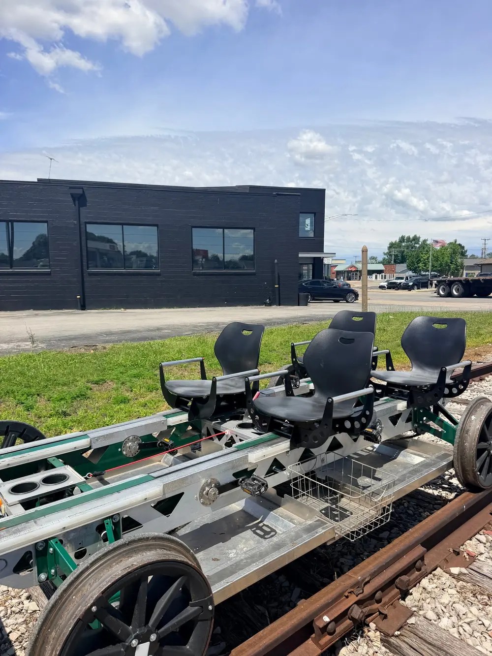 Rail cart on tracks with four black seats, building in background.