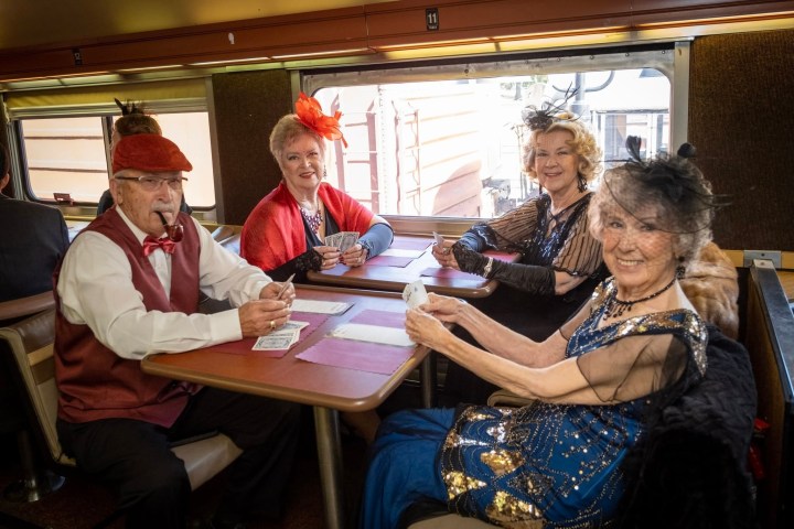 Four people in vintage attire playing cards at a train table.