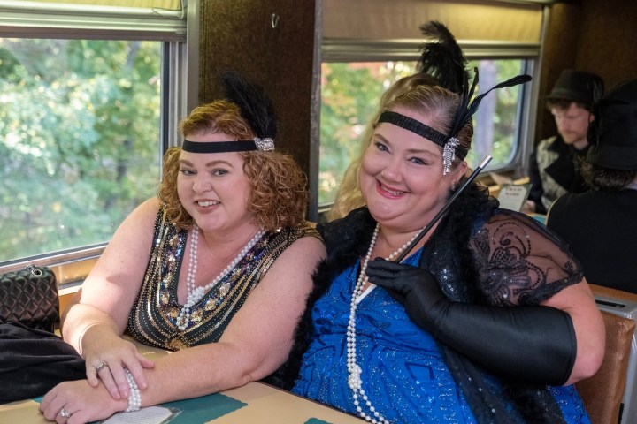 Two women in flapper costumes on a train, smiling.