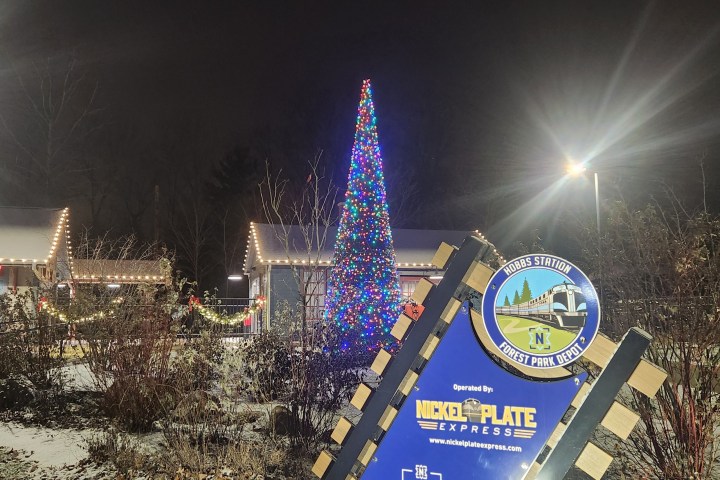Snowy scene with festive lights and a tall Christmas tree near a Nickel Plate Express sign.