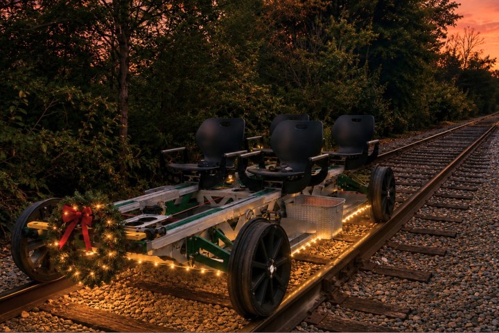 Rail cart with holiday lights and wreath on train tracks at sunset.